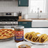 Dylan's Hot Honey jar on a kitchen counter with pizza and tacos.