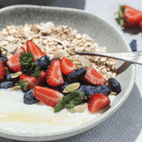 Colorful bowl of yogurt topped with strawberries, blueberries, oats, and mint leaves, showcasing a healthy breakfast option.