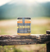 a jar of Welsh wildflower honey resting on a rustic fence with fields and hills behind