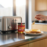 Person drizzling honey onto toast with a jar of honey in the background